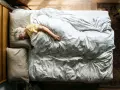 Eine ältere Frau schläft tief und fest in einem gemütlichen Bett. Wenn alte Menschen viel schlafen, ist das oft ein Zeichen von Ruhe und Erholung.