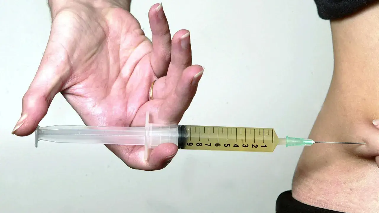 Hand hält Spritze mit gelber Flüssigkeit, bereit zur Injektion. Mögliche Verkapselung nach Thrombosespritze.