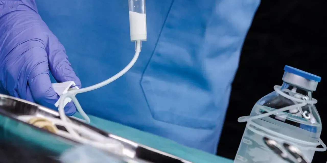 Arzt mit Handschuh bereitet Infusion vor. Ein Tropfbehälter und eine Medikamentenflasche sind zu sehen. Sondieren medizin.
