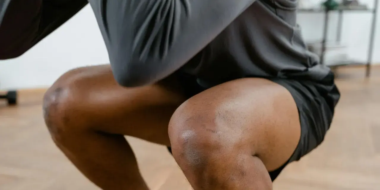Mann in Sportkleidung macht Kniebeugen. Bei Schmerzen in der Kniekehle welcher Arzt ist der richtige Ansprechpartner?