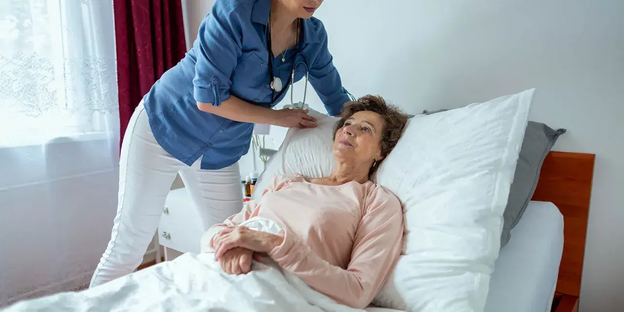 Pflegekraft unterstützt ältere Frau im Bett. Die richtige pneumonie lagerung ist wichtig für die Genesung.