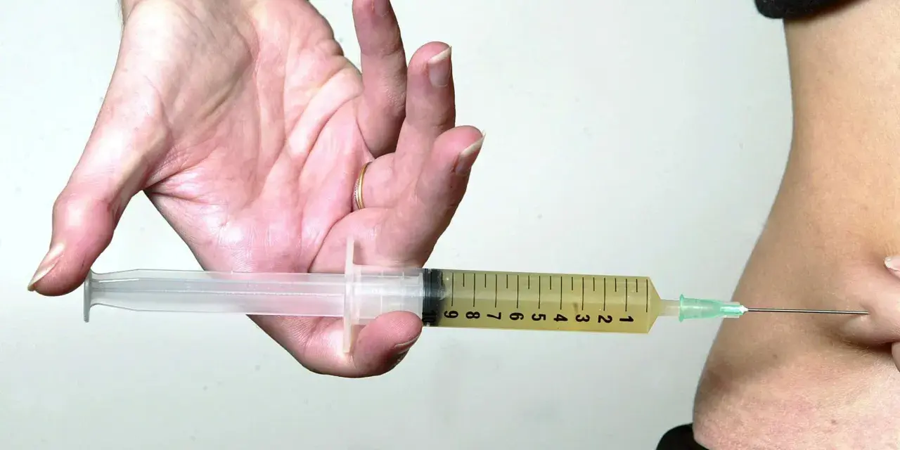 Hand hält Spritze mit gelber Flüssigkeit, bereit zur Injektion. Mögliche Verkapselung nach Thrombosespritze.