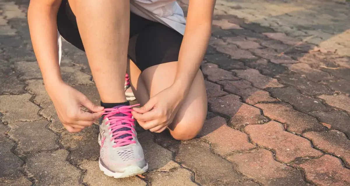 Frau bindet Schnürsenkel ihrer Laufschuhe. Nach einer Thrombose ist die Frage "wie lange kein Sport" wichtig für die Genesung.