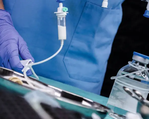 Arzt mit Handschuh bereitet Infusion vor. Ein Tropfbehälter und eine Medikamentenflasche sind zu sehen. Sondieren medizin.