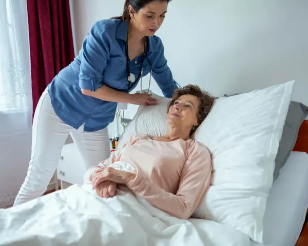 Pflegekraft unterstützt ältere Frau im Bett. Die richtige pneumonie lagerung ist wichtig für die Genesung.
