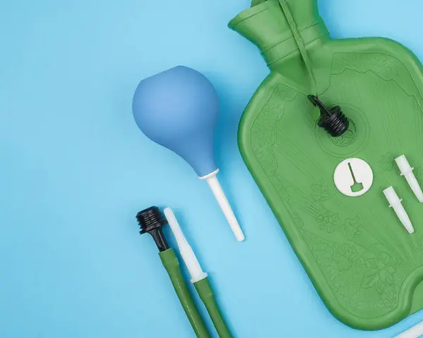 Grüne Wärmflasche mit Zubehör für einen hebe schwenkeinlauf. Blaue Birne und grüne Schläuche mit Aufsätzen liegen daneben.