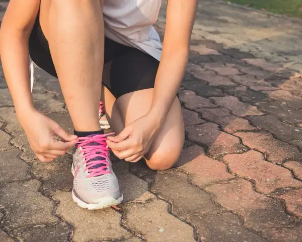 Frau bindet Schnürsenkel ihrer Laufschuhe. Nach einer Thrombose ist die Frage "wie lange kein Sport" wichtig für die Genesung.