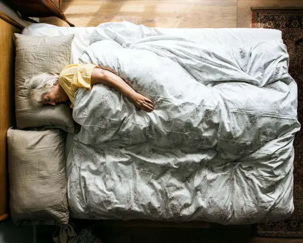 Eine ältere Frau schläft tief und fest in einem gemütlichen Bett. Wenn alte Menschen viel schlafen, ist das oft ein Zeichen von Ruhe und Erholung.