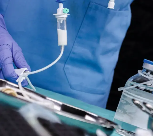 Arzt mit Handschuh bereitet Infusion vor. Ein Tropfbehälter und eine Medikamentenflasche sind zu sehen. Sondieren medizin.