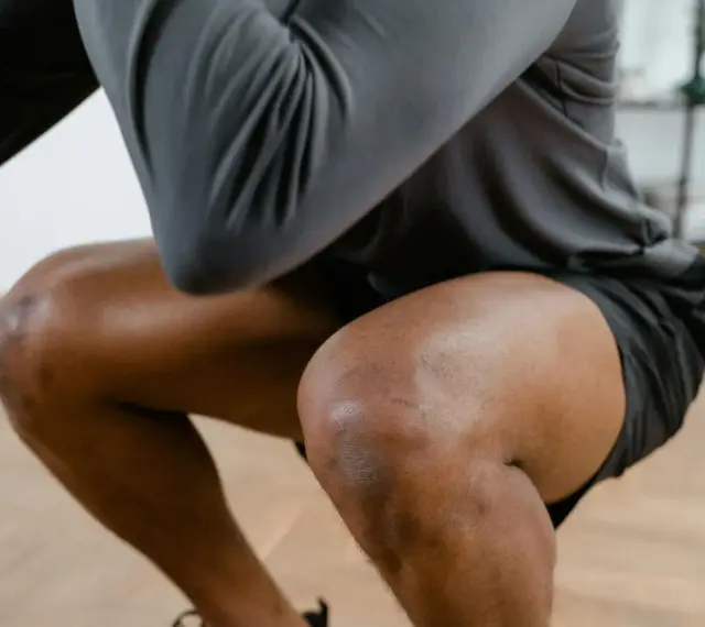 Mann in Sportkleidung macht Kniebeugen. Bei Schmerzen in der Kniekehle welcher Arzt ist der richtige Ansprechpartner?