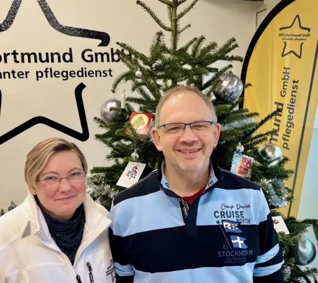 Zwei Mitarbeiter des ambulanten Pflegedienstes APD Dortmund stehen vor einem Weihnachtsbaum. Bei Fragen zum pflegedienst beschwerdestelle nrw sind sie gerne für Sie da.