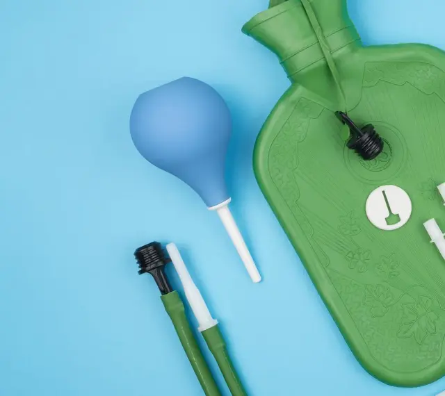 Grüne Wärmflasche mit Zubehör für einen hebe schwenkeinlauf. Blaue Birne und grüne Schläuche mit Aufsätzen liegen daneben.