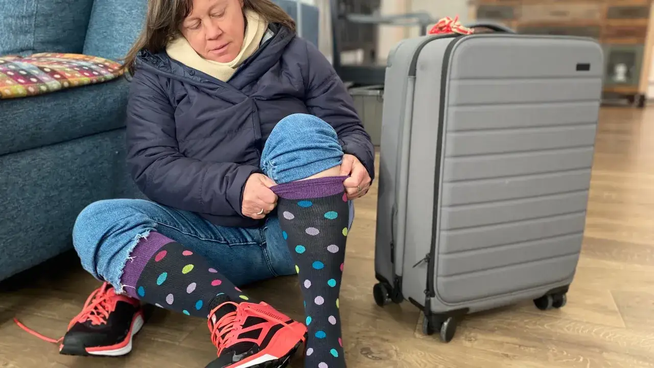Frau zieht Kompressionsstrümpfe an, um mit Thrombose zu fliegen. Gepäck steht bereit.