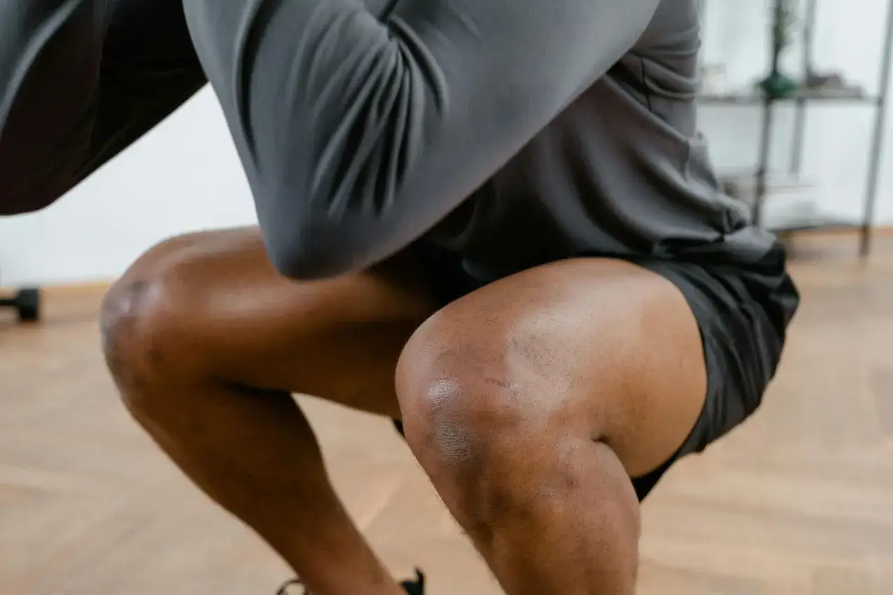 Sportler mit Schmerzen in der Kniekehle: Welcher Arzt hilft? Ein Mann in Sportkleidung macht eine Kniebeuge.