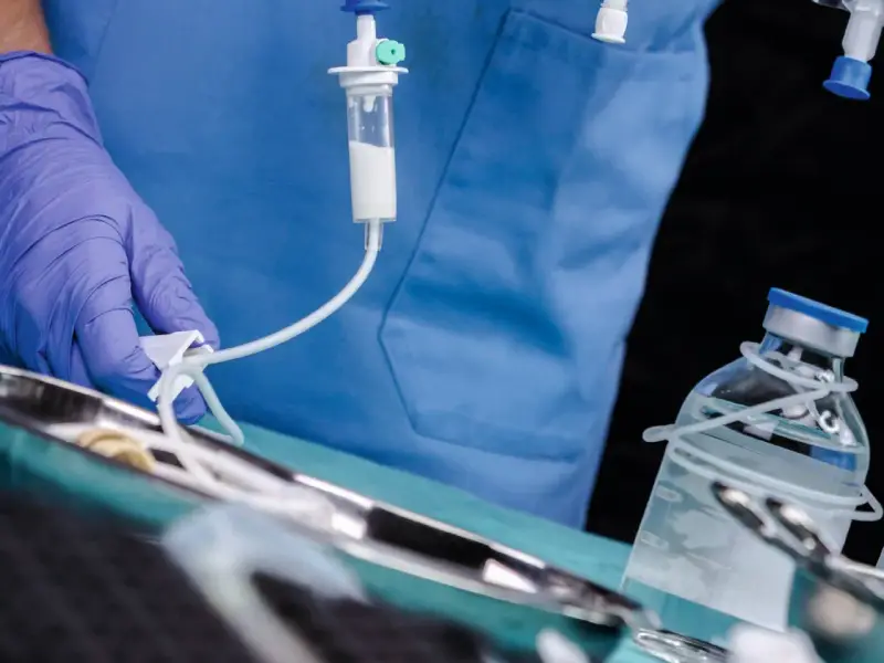 Arzt mit Handschuh bereitet Infusion vor. Ein Tropfbehälter und eine Medikamentenflasche sind zu sehen. Sondieren medizin.