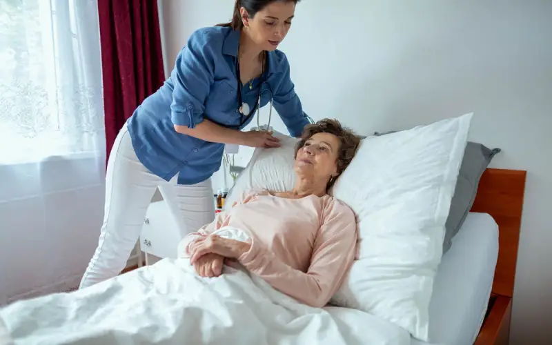 Pflegekraft unterstützt ältere Frau im Bett. Die richtige pneumonie lagerung ist wichtig für die Genesung.