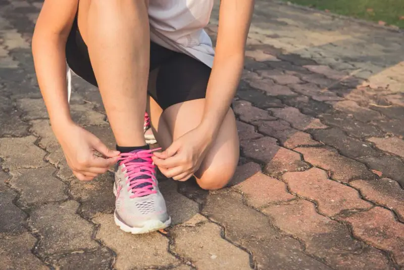 Frau bindet Schnürsenkel ihrer Laufschuhe. Nach einer Thrombose ist die Frage "wie lange kein Sport" wichtig für die Genesung.